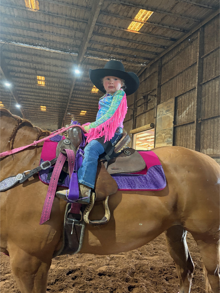 A young cowgirl mounted and ready to compete in the indoor arena